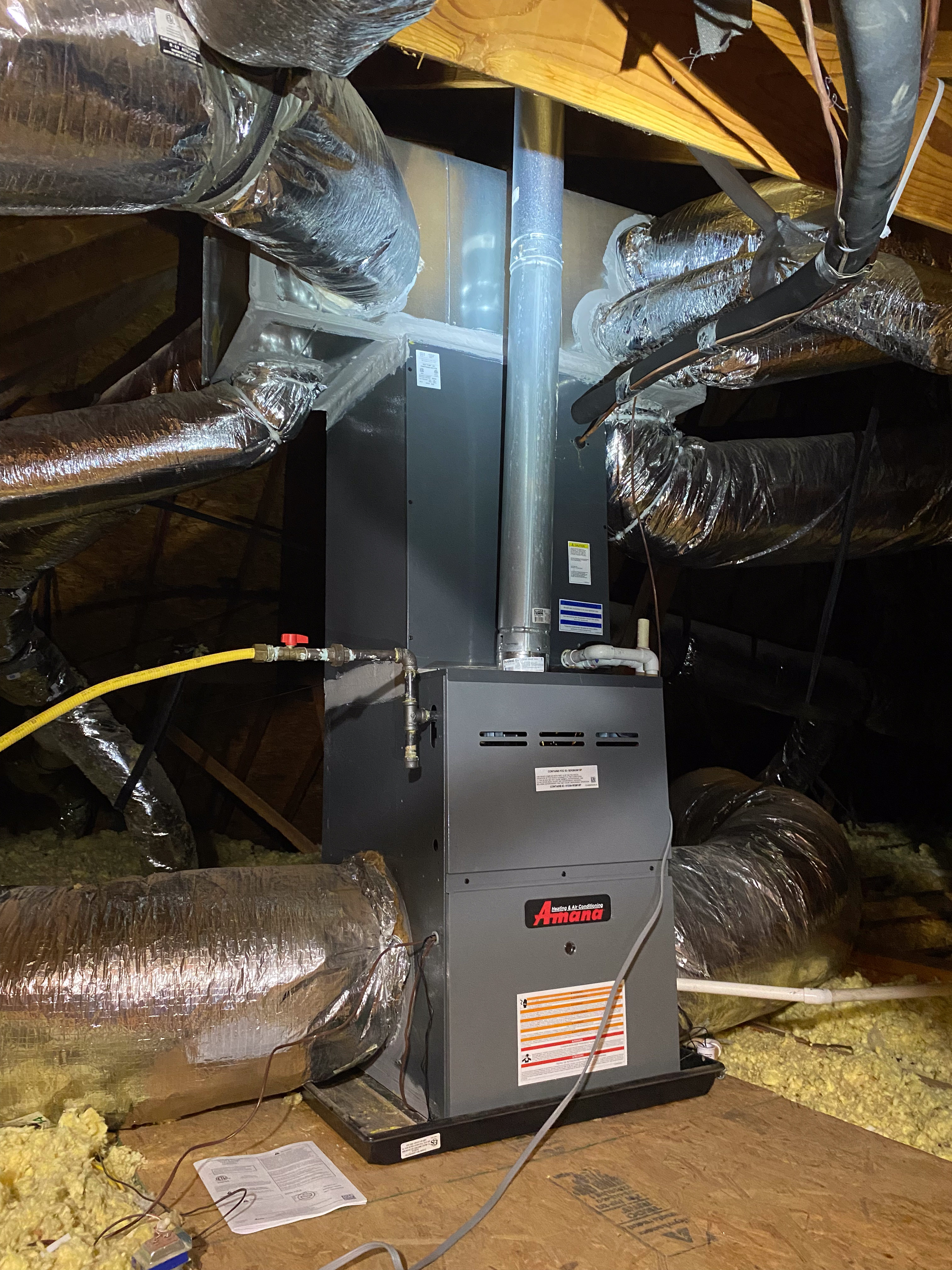 HVAC technician using a manifold gauge to check refrigerant levels on an outdoor air conditioning unit with exposed wiring and components.