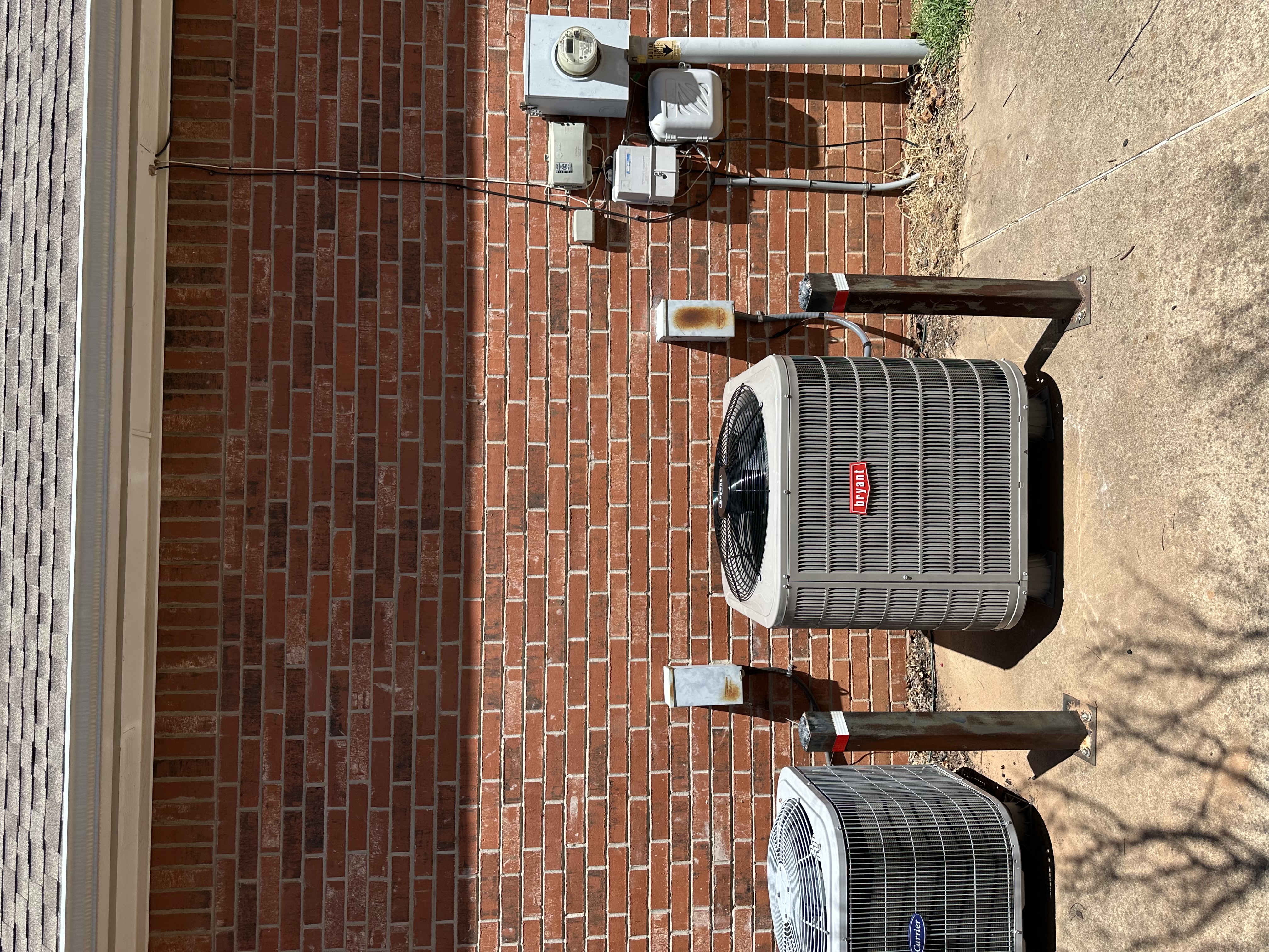 HVAC technician using a manifold gauge to check refrigerant levels on an outdoor air conditioning unit with exposed wiring and components.